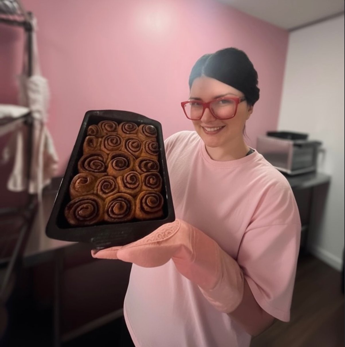 Kelsea, founder of The Blushing Crumb, holding a fresh tray of cinnamon rolls